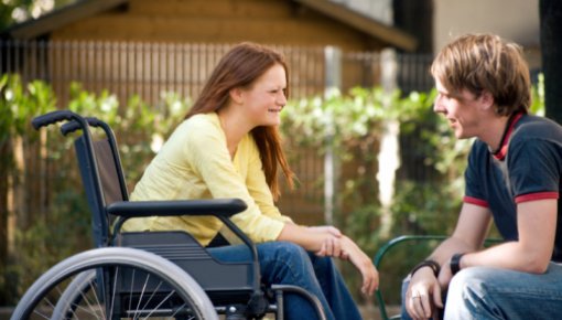 Photo of a young woman in a wheelchair talking to a friend