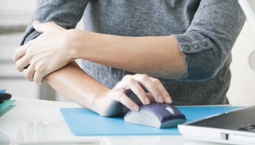 Photo of a woman with elbow pain at a computer