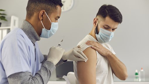 Photo of doctor with face mask vaccinating male patient