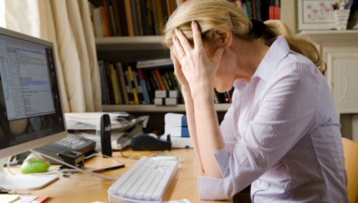 Photo of woman sitting at a desk, holding her head in her hands