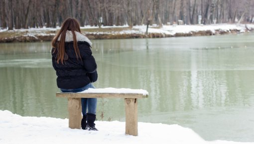 Photo of woman sitting by a wintry lake