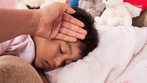 Photo of an adult's hand against a sleeping child's forehead