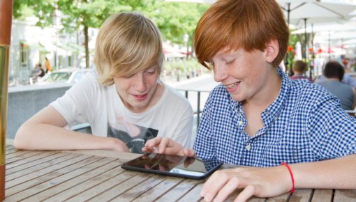 Photo of two teenagers using a tablet device outside on a sunny day