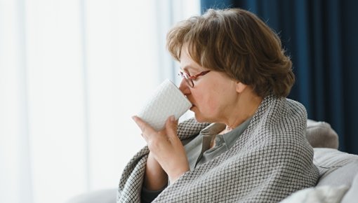 Photo: Elderly lady wrapped in a blanket in an armchair, drinking from a mug