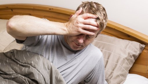 Photo of a man in bed holding his head in pain