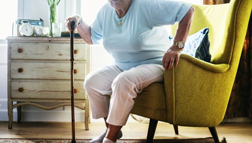 Elderly lady with a walking stick getting out of an armchair