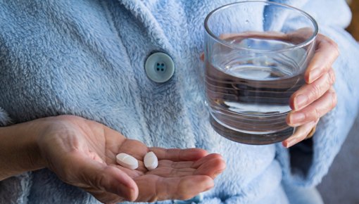 Elderly woman holding pills and a glass of water