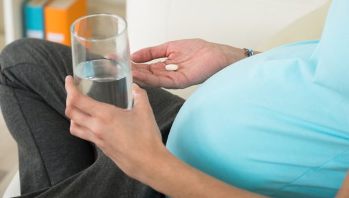 A pregnant woman sitting down, taking tablets with a glass of water