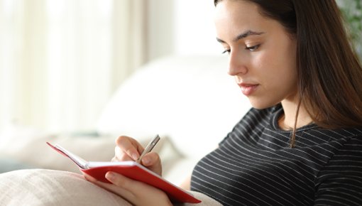 Photo of a young woman on a sofa, writing in a diary