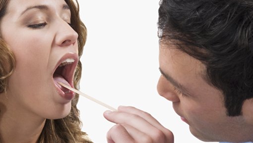 Photo of a patient having their mouth and throat examined by a doctor