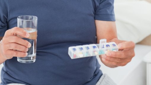 Man with glass of water and box of tablets taking medication